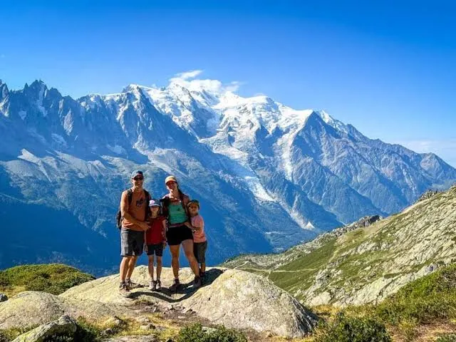 A smiling family of four standing on a rock in front of snowy mountains